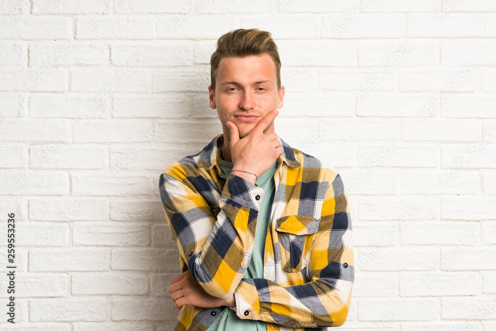 Blonde handsome man over white brick wall standing and thinking an idea Blonde handsome man over white brick wall standing and thinking an idea
