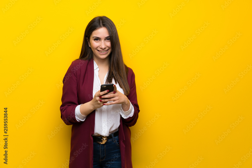 Young woman over yellow wall sending a message with the mobile Young woman over yellow wall sending a message with the mobile