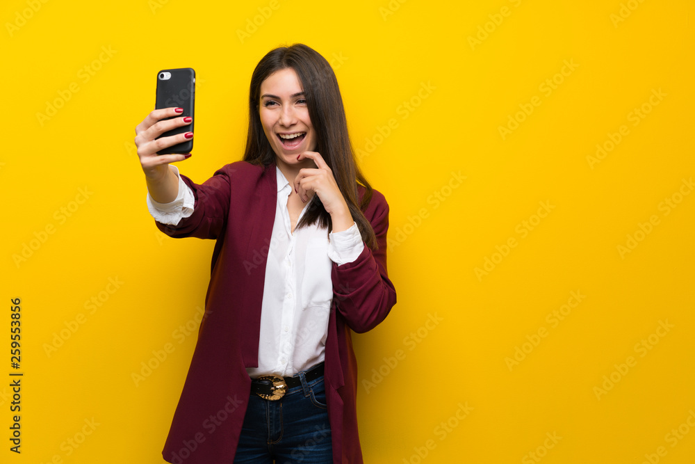 Young woman over yellow wall making a selfie Young woman over yellow wall making a selfie