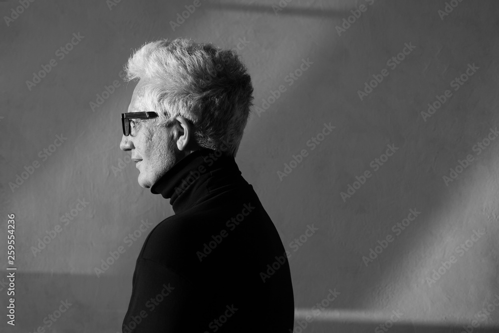 Never get old, handsome and sexy at every age concept. Profile portrait of fashionable mature man wearing trendy eyewear, black turtleneck. Modern haircut. Silver hair. Daylight. Graphic shadows Never get old, handsome and sexy at every age concept. Profile portrait of fashionable mature man wearing trendy eyewear, black turtleneck. Modern haircut. Silver hair. Daylight. Graphic shadows