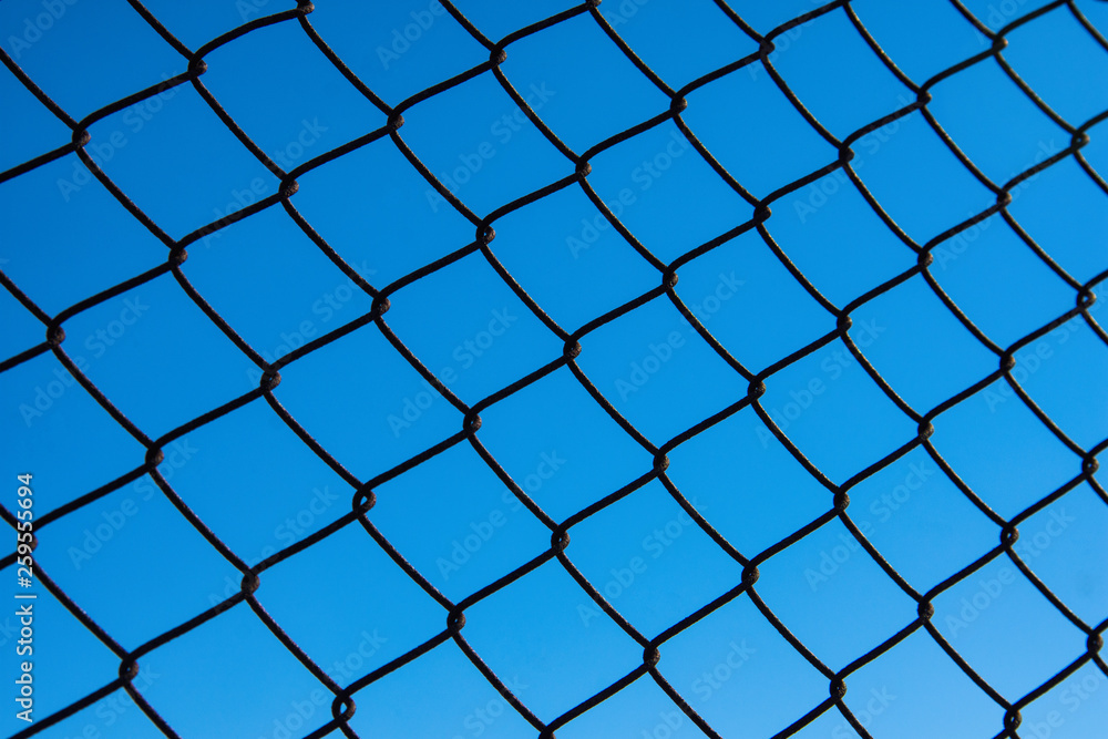 Metal black fence-mesh netting against a clear blue sky. The background image of the fence. Metal black fence-mesh netting against a clear blue sky. The background image of the fence.