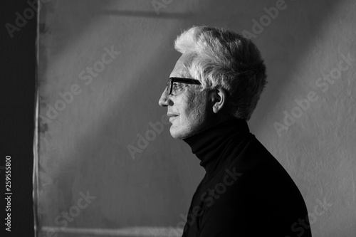 Wallpaper Mural Never get old, handsome and sexy at every age concept. Portrait of fashionable mature man wearing trendy eyewear, black turtleneck, sitting in art gallery. Modern haircut. Silver hair. Graphic shadows Torontodigital.ca