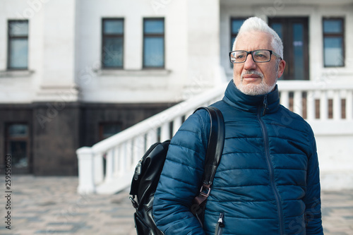 Active retirement concept. Portrait of handsome silver haired mature man watching signtseeing attractions in center of old European capital city. Nice winter day. Modern haircut, beard. Outdoor shot photo