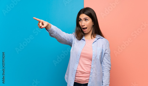 Young woman over pink and blue wall pointing away