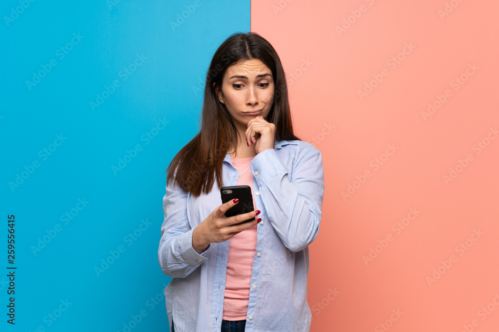 Young woman over pink and blue wall celebrating a victory with a mobile Young woman over pink and blue wall celebrating a victory with a mobile