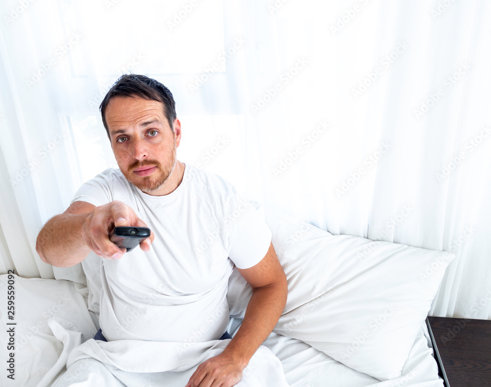 Man using remote control while sitting in the bed at home and watching TV in the morning. Man using remote control while sitting in the bed at home and watching TV in the morning.