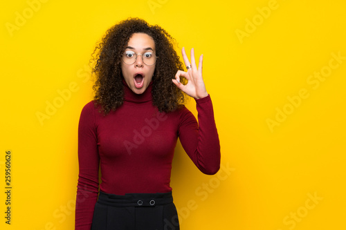 Dominican woman with turtleneck sweater surprised and showing ok sign