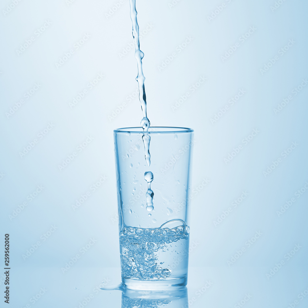 Pouring water into glass on white background. Water spilled on the table.