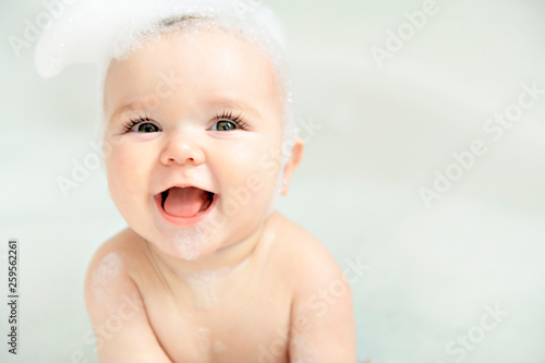 Tableau sur Toile A Baby girl bathes in a bath with foam and soap bubbles