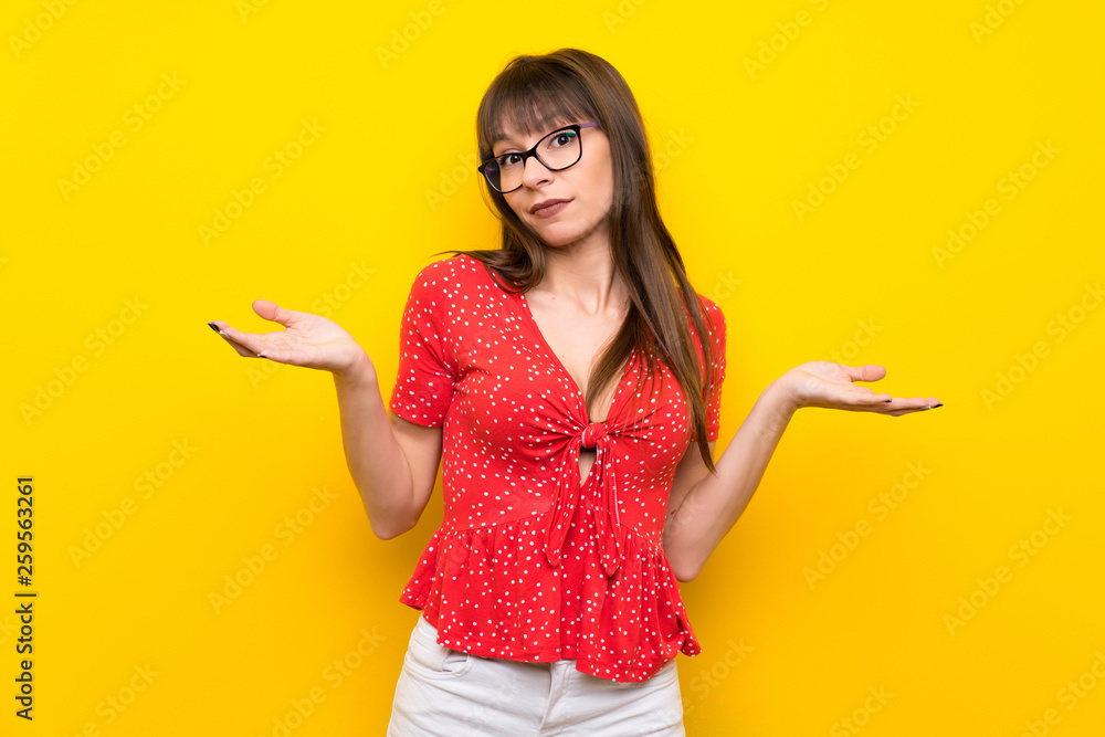 Young woman over yellow wall making doubts gesture Young woman over yellow wall making doubts gesture