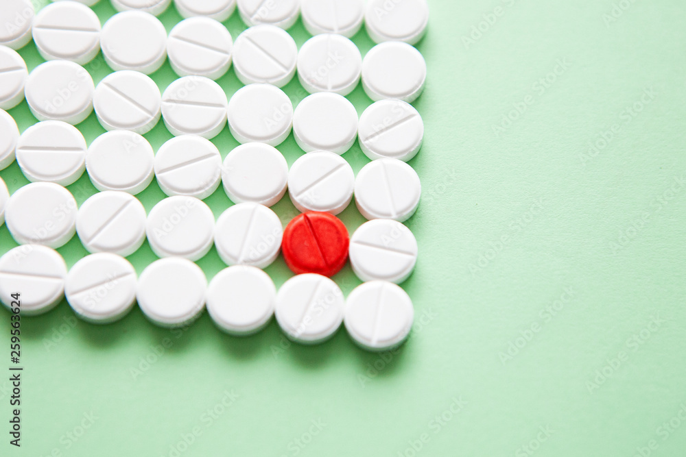Top view of a pile of white medicine pills on a white surface. One tablet of red medication. Vaccine concept