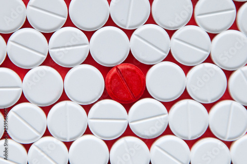 Top view of a pile of white medicine pills on a white surface. One tablet of red medication. Vaccine concept photo