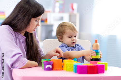 Cute woman and kid boy playing educational toys at kindergarten or nursery room