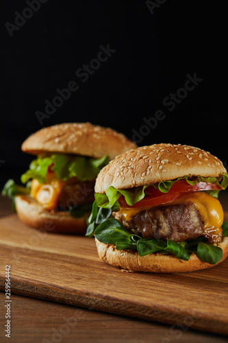 selective focus of tasty meat burgers on wooden chopping board isolated on black