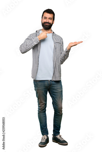 Handsome man with beard holding copyspace imaginary on the palm to insert an ad over isolated white background
