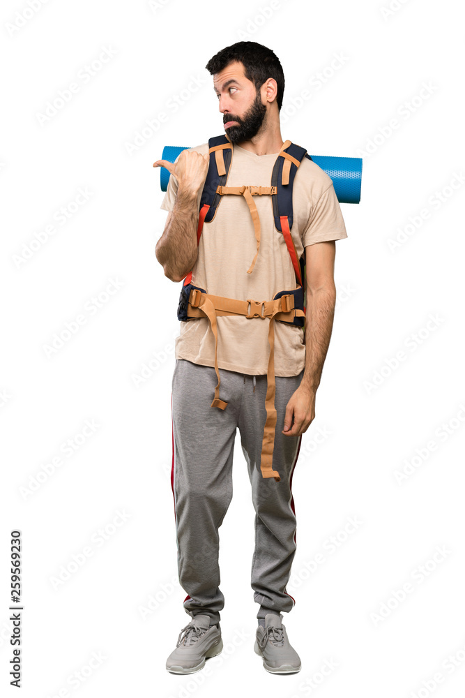 Hiker man unhappy and pointing to the side over isolated white background Hiker man unhappy and pointing to the side over isolated white background