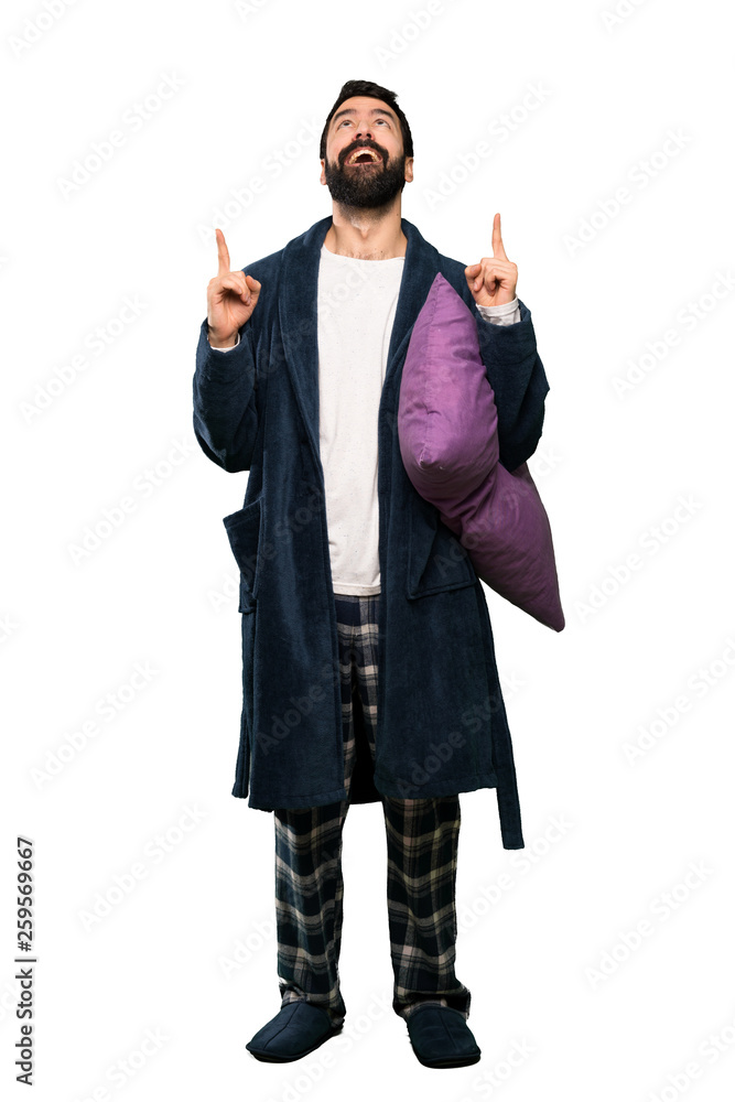 Man with beard in pajamas surprised and pointing up over isolated white background Man with beard in pajamas surprised and pointing up over isolated white background