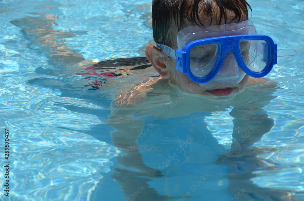 Naklejka premium Teenager boy wearing mask swimming in the pool. Happy holiday concept. Cute happy little boy swimming and snorking in the sea ocean in crystal blue water