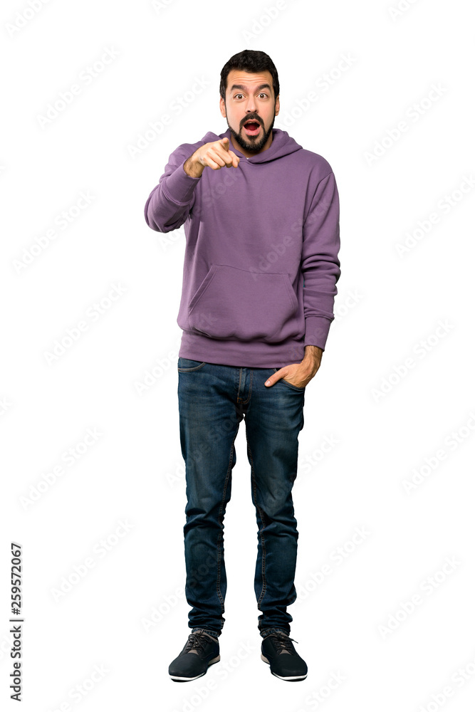 Naklejka premium Full-length shot of Handsome man with sweatshirt surprised and pointing front over isolated white background