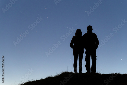 Silhouettes of young man and young woman holding hands and a blue starry sky on the background