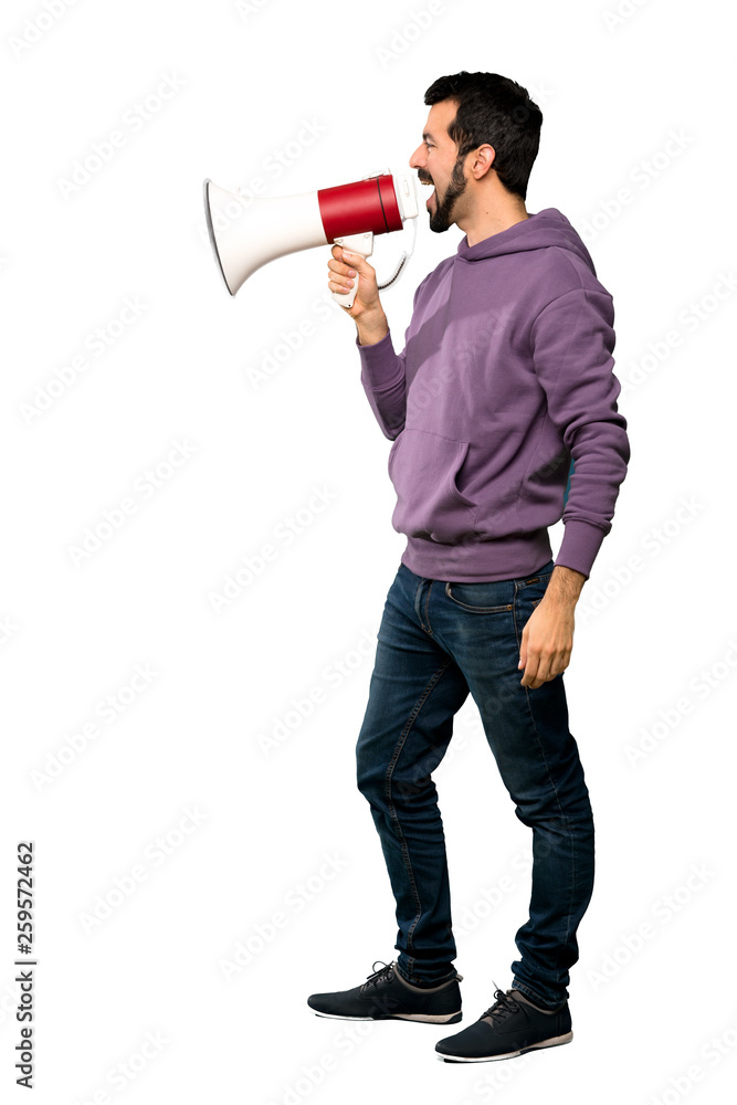 Full-length shot of Handsome man with sweatshirt shouting through a megaphone over isolated white background Full-length shot of Handsome man with sweatshirt shouting through a megaphone over isolated white background