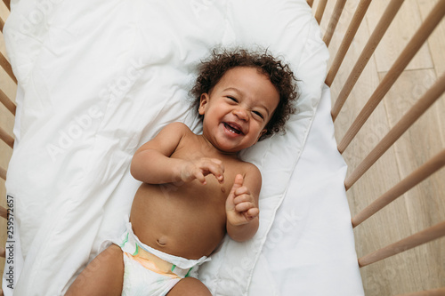 Laughing baby boy lying in a crib wearing a diaper