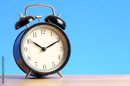 Black alarm clock on the wooden surface against the blue background.