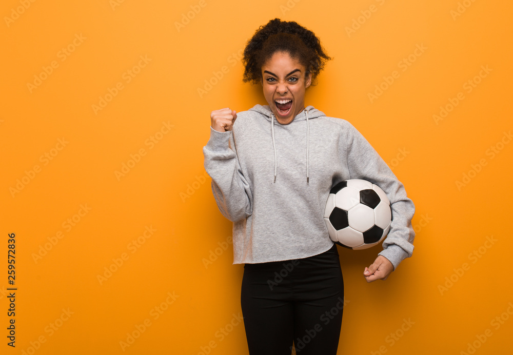 Young fitness black woman screaming very angry and aggressive. Holding a soccer ball. Young fitness black woman screaming very angry and aggressive. Holding a soccer ball.