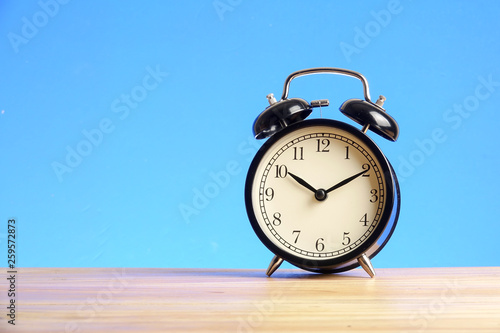 Black alarm clock on the wooden surface against the blue background.