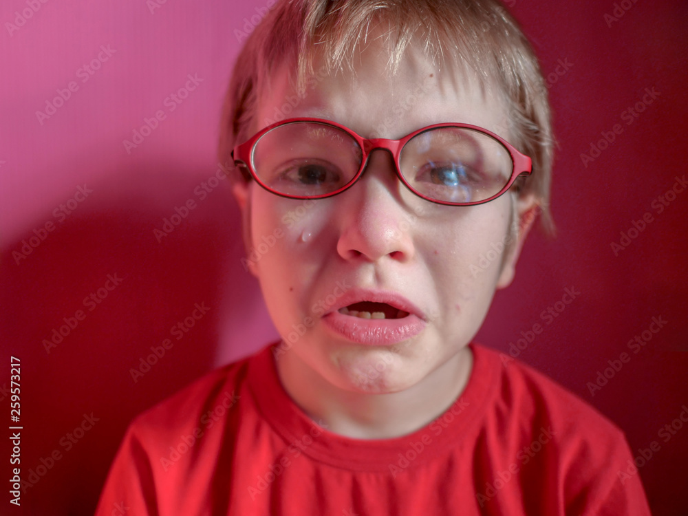 Upset child in red sweater on red background is crying and actively expresses emotions. Close up little kid boy in glasses crying with tearful on her face Upset child in red sweater on red background is crying and actively expresses emotions. Close up little kid boy in glasses crying with tearful on her face