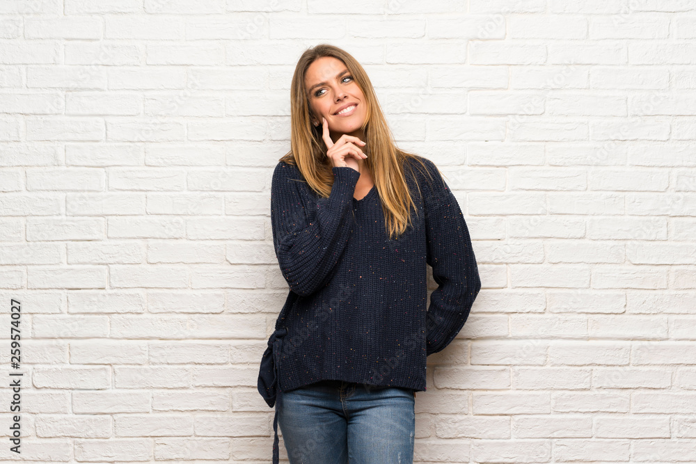 Blonde woman over brick wall thinking an idea pointing the finger up Blonde woman over brick wall thinking an idea pointing the finger up
