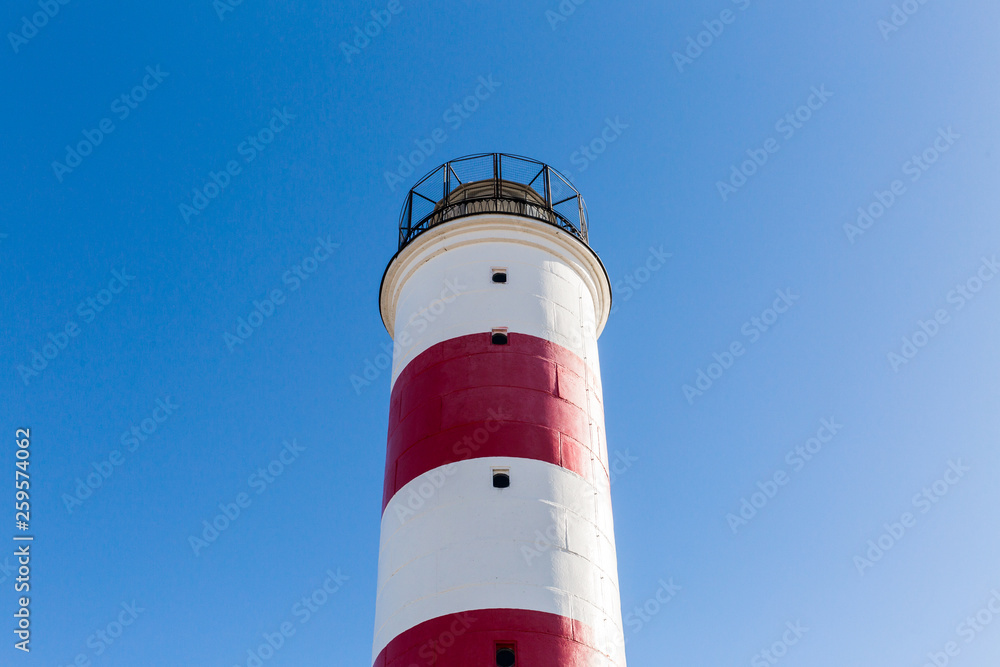 white and red striped beacon on the coastline on blue sky background. lighthouse
