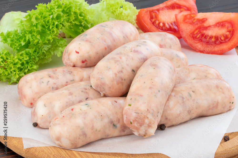 Fresh raw sausage with lettuce and tomato on the wooden background Fresh raw sausage with lettuce and tomato on the wooden background