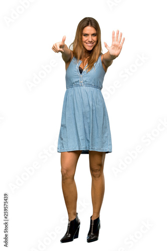 A full-length shot of a Blonde woman with jean dress counting six with fingers over isolated white background