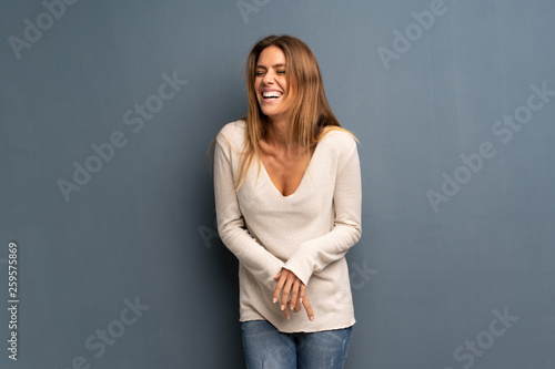 Blonde woman over grey background smiling a lot