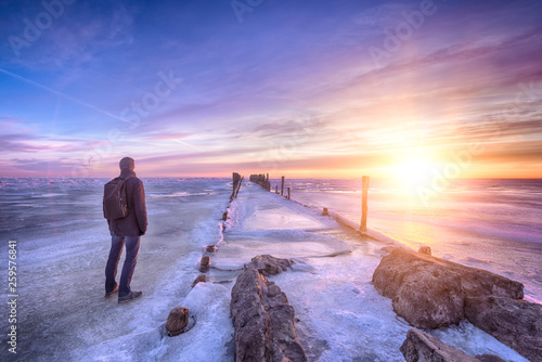 Winter seascape of wood breakwaters and traveller on frozen Baltic sea