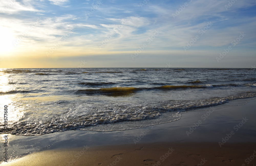 Sunset over the Ocean - View of the red sun sinking into the horizon and waves washing over the sand of the beach