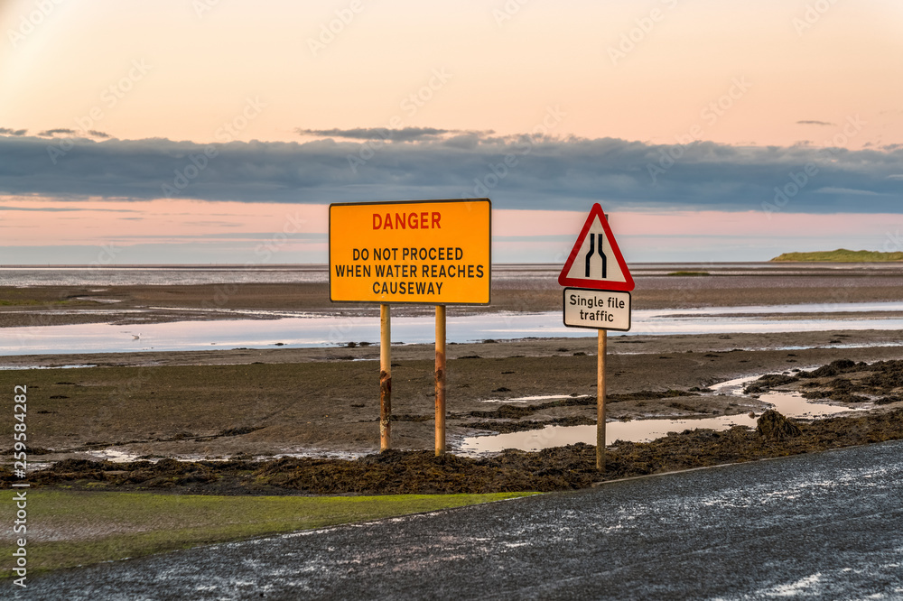 Sign: Single File Traffic, Danger do not proceed when water reaches causeway, seen on the road between Beal and Holy Island in Northumberland, England, UK