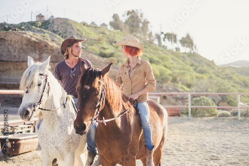 Happy smiling couple doing a horse riding togethe rin the nature - outdoor leisure activity for young people together in friendship with animals for therapy © simona
