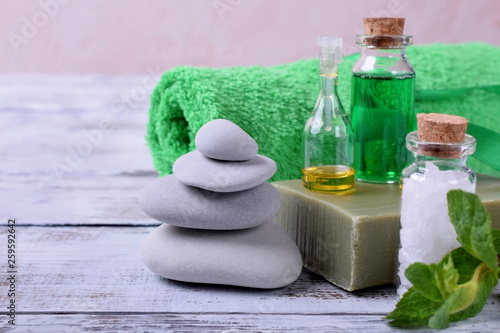 Spa set: massage stones, aromatic oil, sea salt, green gel, organic soap and green towel on white wooden table