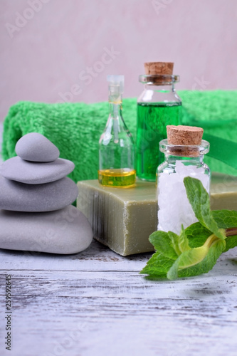 Spa set  massage stones  aromatic oil  sea salt  green gel  organic soap and green towel on white wooden table