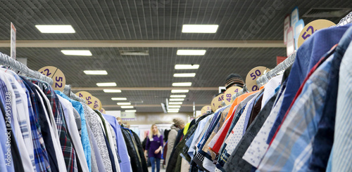 Elegant shirts hanging in two rows on hangers in the store are blurry. In the background are blurred buyers. On the eve of Black Friday. Background for design from a department store.