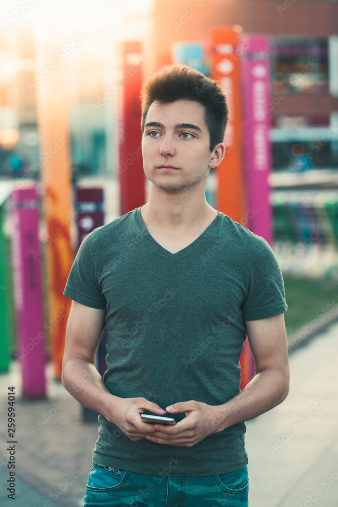 Young man holding smartphone, standing on street in center of town Young man holding smartphone, standing on street in center of town