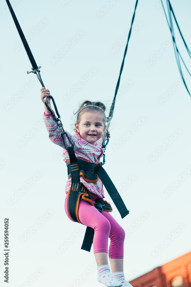 Little adorable smiling girl jumping on trampoline, having fun at funfair