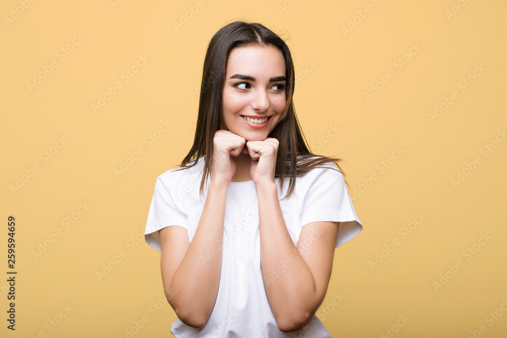 Young attractive long haired woman looking away smiling leaning her chin on her hands isolated on a yellow studio wall. Young attractive long haired woman looking away smiling leaning her chin on her hands isolated on a yellow studio wall.