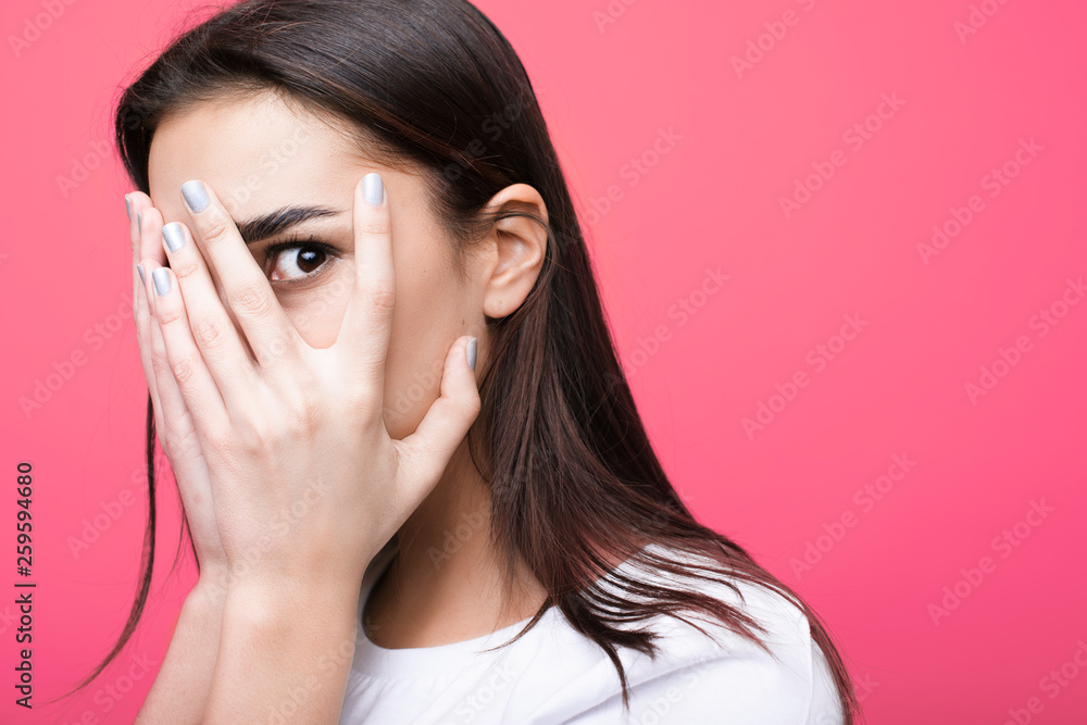 Φωτογραφία Close up portrait of a beautiful woman with dark hair looking through hands on her face isolated on a pink studio wall