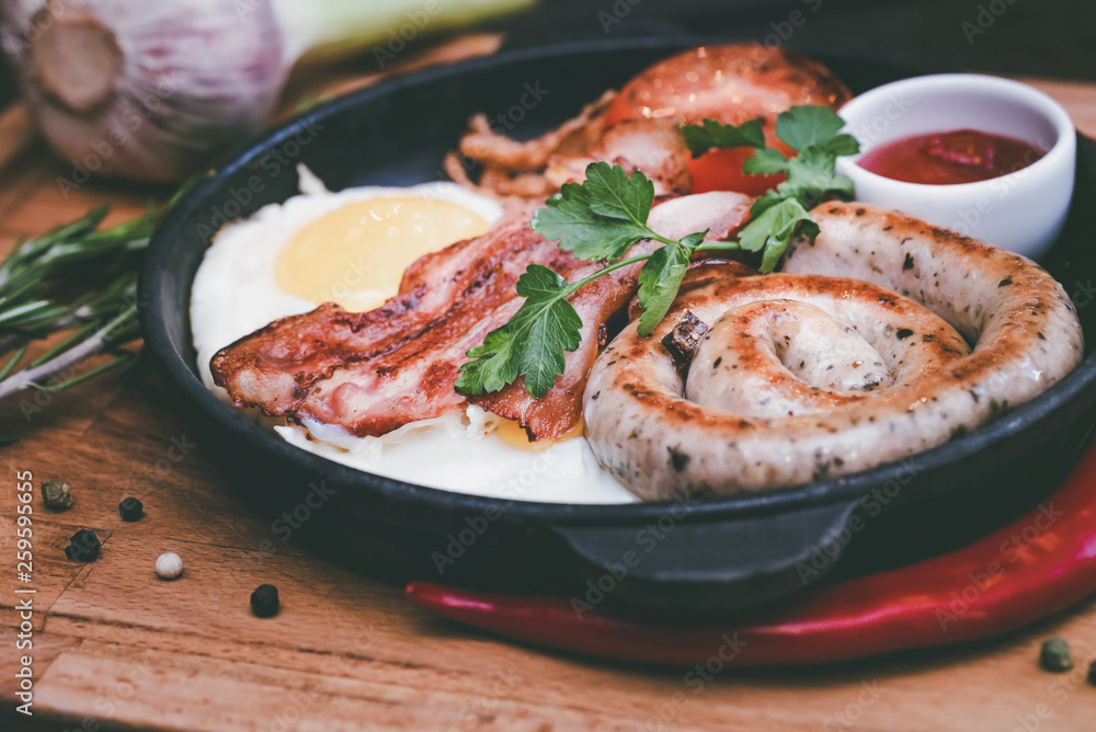 Nutritious meal with fried egg, sausage, bacon, tomato and sauce in frying pan Nutritious meal with fried egg, sausage, bacon, tomato and sauce in frying pan