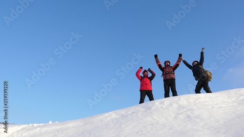 Travelers come to the top of snowy hill and enjoy the victory against the blue sky. teamwork and victory. teamwork of people in difficult conditions. tourists travel in the snow in winter.