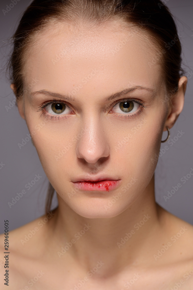 portrait of a young beautiful girl with blood on her lips, on a gray background.