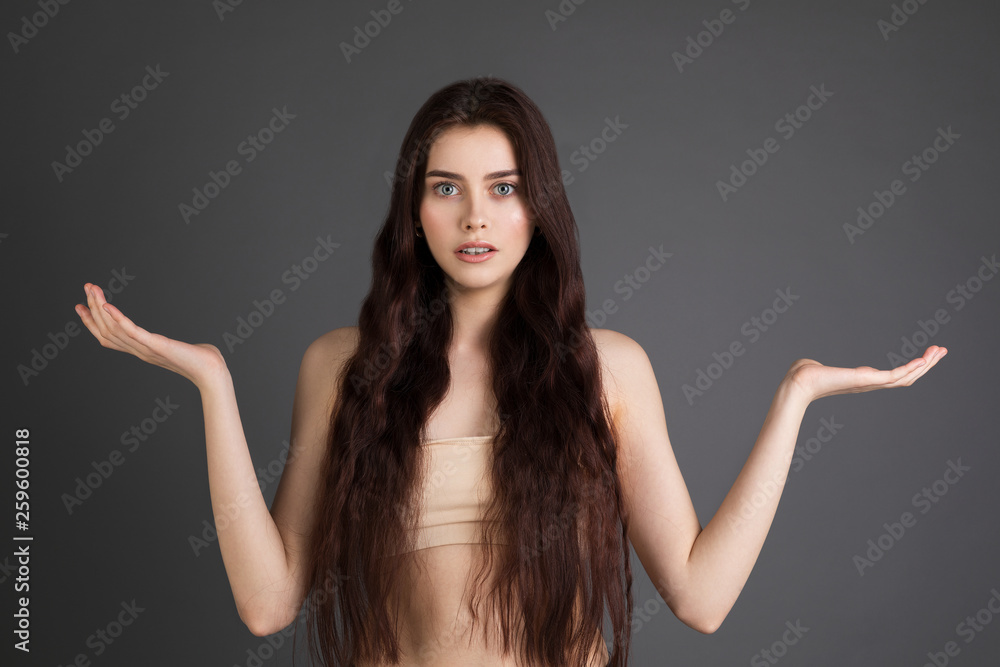 Young brunette girl with bare shoulders pointing hands on side to present a product Young brunette girl with bare shoulders pointing hands on side to present a product